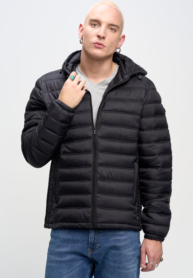 Sort dunjakke med quiltet tekstur, lynlåslukning foran og justerbar hætte. Bæres over en lys grå V-hals skjorte, parret med blå jeans.