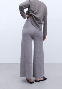 Maglione grigio chiaro lavorato a maglia con maniche lunghe e orlo arrotondato. Pantaloni larghi a vita alta, dal taglio ampio e in una texture grigia abbinata.