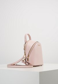 Růžový kožený batoh se strukturovaným tvarem, dvojitými zipy a odnímatelným popruhem. Obsahuje zlaté kovové doplňky a texturovaný povrch.