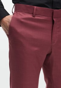 Bordó szabott nadrág texturált anyagból, lapos elülső résszel, övbújtatókkal és oldalsó zsebekkel, slim fit fazonnal.