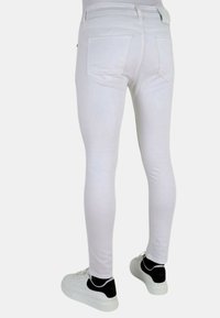 Witte skinny jeans van rekbare stof, met twee achterzakken en een naadloos ontwerp. Gecombineerd met witte sneakers met zwarte accenten.