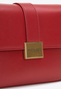 Borsa a mano in pelle rossa con superficie liscia, accessori in oro e un gancio prominente con la scritta "WITTCHEN" incisa. Rifinita con una cucitura.