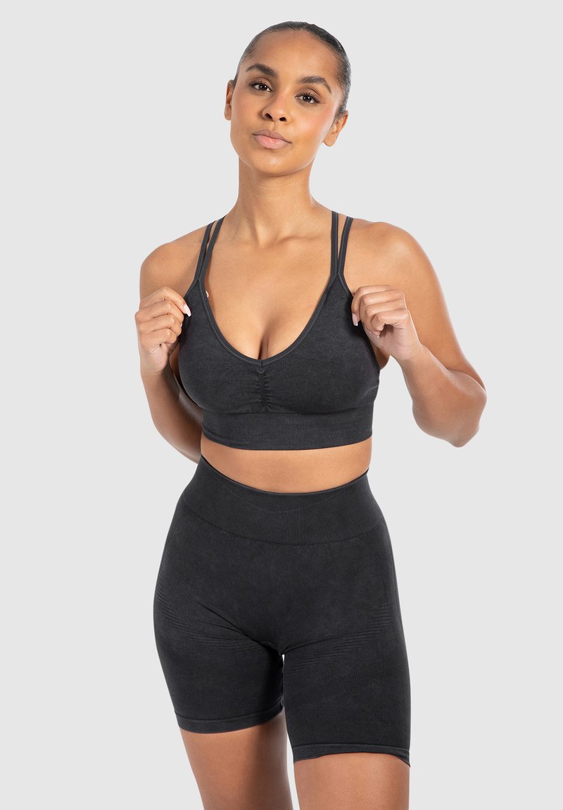 Conjunto deportivo negro que incluye una camiseta corta con escote en V y tirantes ajustables, acompañada de pantalones cortos de tiro alto. El material parece suave con acentos texturizados.