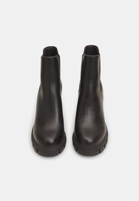 Botines de cuero negro con una superficie lisa, punteras redondeadas y suelas de goma texturizadas. Diseño sin costuras con paneles laterales elásticos.