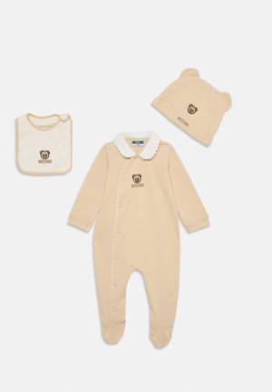 Body de bébé en coton beige avec un col blanc festonné, logo d'ours, bavoir assorti et chapeau avec des oreilles d'ours. Tissu doux, fermeture à pression.
