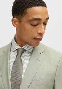 Light green suit with a textured tie in a geometric pattern, paired with a white shirt featuring vertical green stripes.