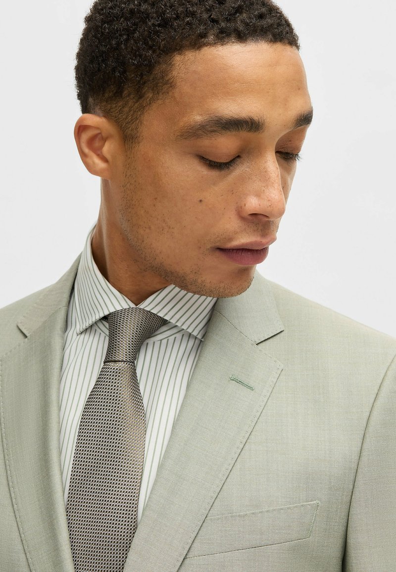 Light green suit with a textured tie in a geometric pattern, paired with a white shirt featuring vertical green stripes.