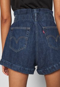 Pantalones cortos de denim oscuro con una cintura alta elástica, dobladillos enrollados y dos bolsillos traseros con el patrón de costura distintivo de Levi's.