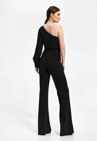 Zwart jumpsuit met een asymmetrisch ontwerp, één lange mouw en één blote schouder, verlengde benen en een aansluitende silhouet.