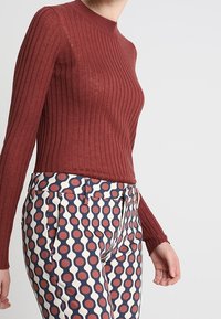 Geribbelde, bordeauxrode lange mouwen top gecombineerd met gestreepte broeken met rode, blauwe en crèmekleurige cirkels; slim fit met een ronde hals.