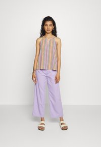 Top de alças com padrão multicolorido e decote em forma de buraco de chave; combinado com calças largas lilás claro e sandálias rasteiras bege.