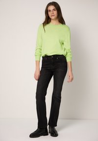 Maglione verde menta a maniche lunghe, abbinato a jeans neri a vita alta e stivaletti neri alla caviglia. Tessuto liscio con taglio aderente.