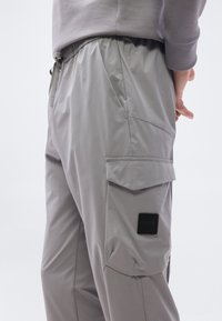 Κοντινή λήψη γκρι παντελονιών φορτίου με ελαστική μέση, μεγάλο καπάκι πλαϊνής τσέπης και μικρό μαύρο λογότυπο BOSS.