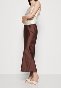 Satin camisole vaalean kerman värisenä yhdistettynä ruskeaan satiini-maxi-hameeseen. Hameessa on sileä pinta ja hieman A-linjainen siluetti.