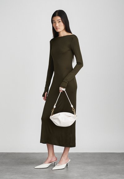 Olīvu zaļš garš piedurkņu kleita ar laivu kakla dizainu, pieguļoša silueta, kopā ar baltu, izliekta dizaina rokassomu un baltām, ar purngaliem uz augšu kājām.