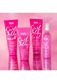Vier haarverzorgingsproducten in roze tubes en een sprayfles. Labels hebben witte tekst; de tubes bevatten Curl Jelly Wash, Care en Scrunching Jelly.