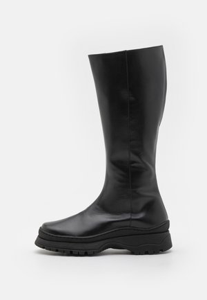 Fekete bőrből készült, a térdig érő csizmák sima felülettel, kerek orral és vastag, mintázott gumitalppal.