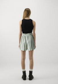 Haut sans manches noir associé à un short taille haute rayé vert et blanc. Le mannequin porte des bottes noires et des chaussettes blanches, vu de dos.