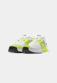 White athletic shoes with green accents, mesh fabric, rubber sole, and lacing system; features a black logo on the side and textured pattern.