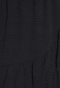 Tissu noir avec une texture à pois en relief, présentant un ourlet froncé. Matériau lisse avec un éclat subtil, créant un effet visuel en couches.