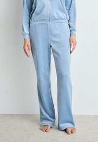 Ljusblå velourbyxor med avslappnad passform och utställd benstruktur, med en mjuk textur och elastisk midja.