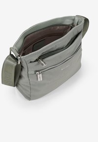 Bolso bandolera de color gris claro, hecho de un tejido suave, que cuenta con un compartimento principal con cremallera y un bolsillo exterior, además de una correa ajustable.