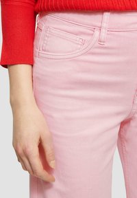Jean rose clair au toucher doux, avec une petite poche avant et des passants de ceinture, associé à un haut rouge à manches longues à côtes.