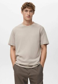 Lysebeige kortærmet t-shirt med rund halsudskæring, glat tekstur og afslappet pasform, kombineret med matchende brune bukser.