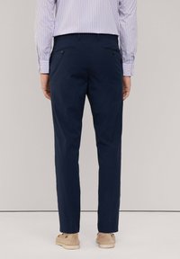 Pantaloni da dress blu navy con finitura testurizzata, dotati di tasche posteriori e vestibilità su misura, abbinati a una camicia button-up a righe.