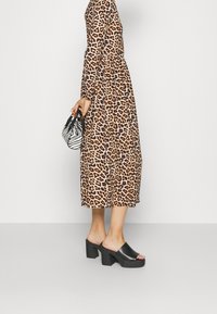 Vestido de manga larga con estampado de leopardo y cintura ceñida, combinado con mules de tacón cuadrado negros. Sosteniendo un bolso a rayas blancas y negras.