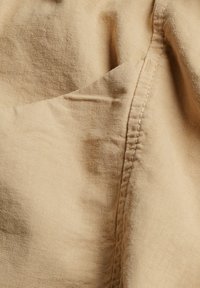 Gros plan sur un tissu beige avec des coutures et des plis visibles, montrant la texture et le détail de la couture.