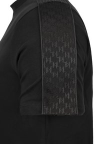 Czarna koszulka z krótkim rękawem z teksturowanym panelem na ramionach z subtelnym geometrycznym wzorem. Gładki materiał i kontrastujące akcenty.