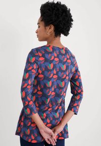 Blusa de manga larga con fondo azul marino y un patrón de hojas coloridas en rojo, verde y azul; material suave y diseño de dobladillo curvado.