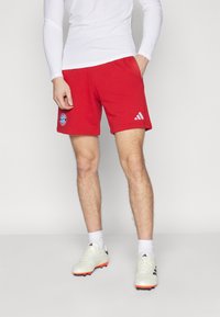 Shorts de sport rouges avec une taille élastique, ornés d'un logo du Bayern Munich et de rayures blanches Adidas sur les côtés.