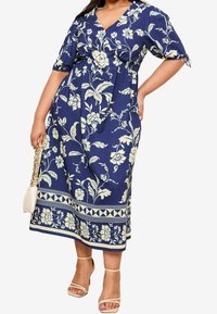 Tmavě modré květinové šaty s krátkými, vyhrnutými rukávy, výstřihem do V a řaseným pasem; mají bílý květinový vzor a vzorovaný lem.