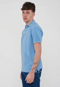 Polo shirt azzurro chiaro in cotone, con colletto classico, patta con tre bottoni e rifiniture bianche a contrasto su maniche e orlo.