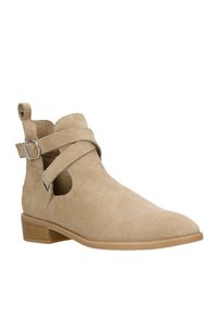 Stivale alla caviglia in suede beige con punta appuntita, lati rinforzati e cinturini incrociati. Presenta un tacco basso impilato e dettagli con fibbia in argento.