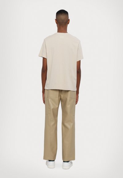 Beige cotton t-shirt with short sleeves paired with beige, wide-legged trousers featuring front pockets and a smooth texture. White shoes complete the look.