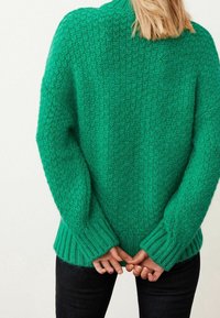 Groene gebreide trui met een textuurpatroon, voorzien van geribde boorden en zoom. De achterkant toont een ontspannen pasvorm en heeft een iets oversized ontwerp.
