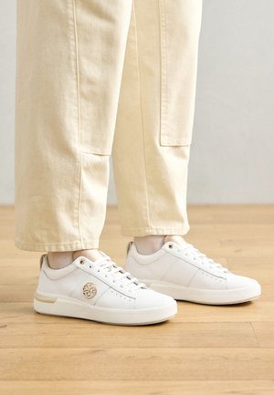 Baskets blanches avec une finition en cuir lisse, bout rond, accents dorés et design à lacets. Présente un logo sur le côté et de subtils perforations.
