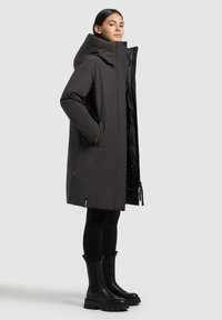 Črn dolg plašč z zadrgo in stranskimi žepi, ki ima kapuco in sijočo notranjost. Uporablja se nad črnimi leginami in debelimi čevlji s peto.