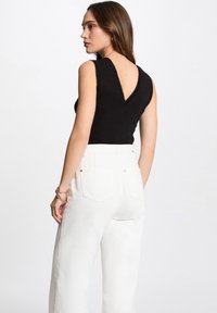 Top nero senza maniche con retro a V e bordi scallop, abbinato a pantaloni bianchi a vita alta. Tessuto morbido e design aderente.