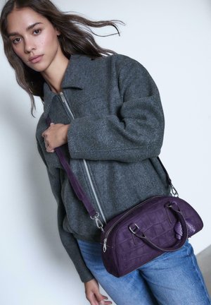 Borsa a tracolla in pelle viola con motivo a coccodrillo texture, manici doppi e tracolla staccabile, abbinata a una giacca grigia con zip.