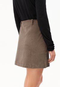 Kastanjebruine corduroy minirok met subtiele verticale ribbels, zijzakken en riemlussen, gecombineerd met een zwart langmouwtop.