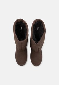 Pari di stivali in suede marrone per l'inverno con rivestimento in pelliccia nera, visti dall'alto, su uno sfondo bianco.