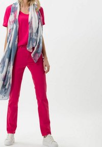 Fuchsiové bavlněné tričko a odpovídající slim-fit kalhoty, doplněné lehkým, vzorovaným šátkem v modré, růžové a bílé barvě. Bílé tenisky.