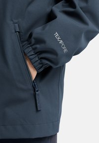 Giacca blu navy realizzata in un tessuto liscio e resistente all'acqua. Presenta una tasca con zip e polsini elasticizzati con il marchio "TEXAPORE".