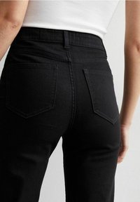 Jeans de mezclilla negra con un diseño ajustado, cintura de corte medio y dos bolsillos traseros con costuras en contraste. Textura suave.