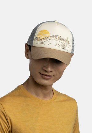 Mann trägt beige und graue Baseballkappe mit Wüstenlandschaft und Sonnendesign, kombiniert mit senfgelbem Hemd, vor hellem Hintergrund.