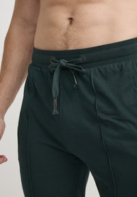 Donkergroene joggerpants van zachte stof, met een elastische tailleband en touwtje, zijzakken en gestikte details.